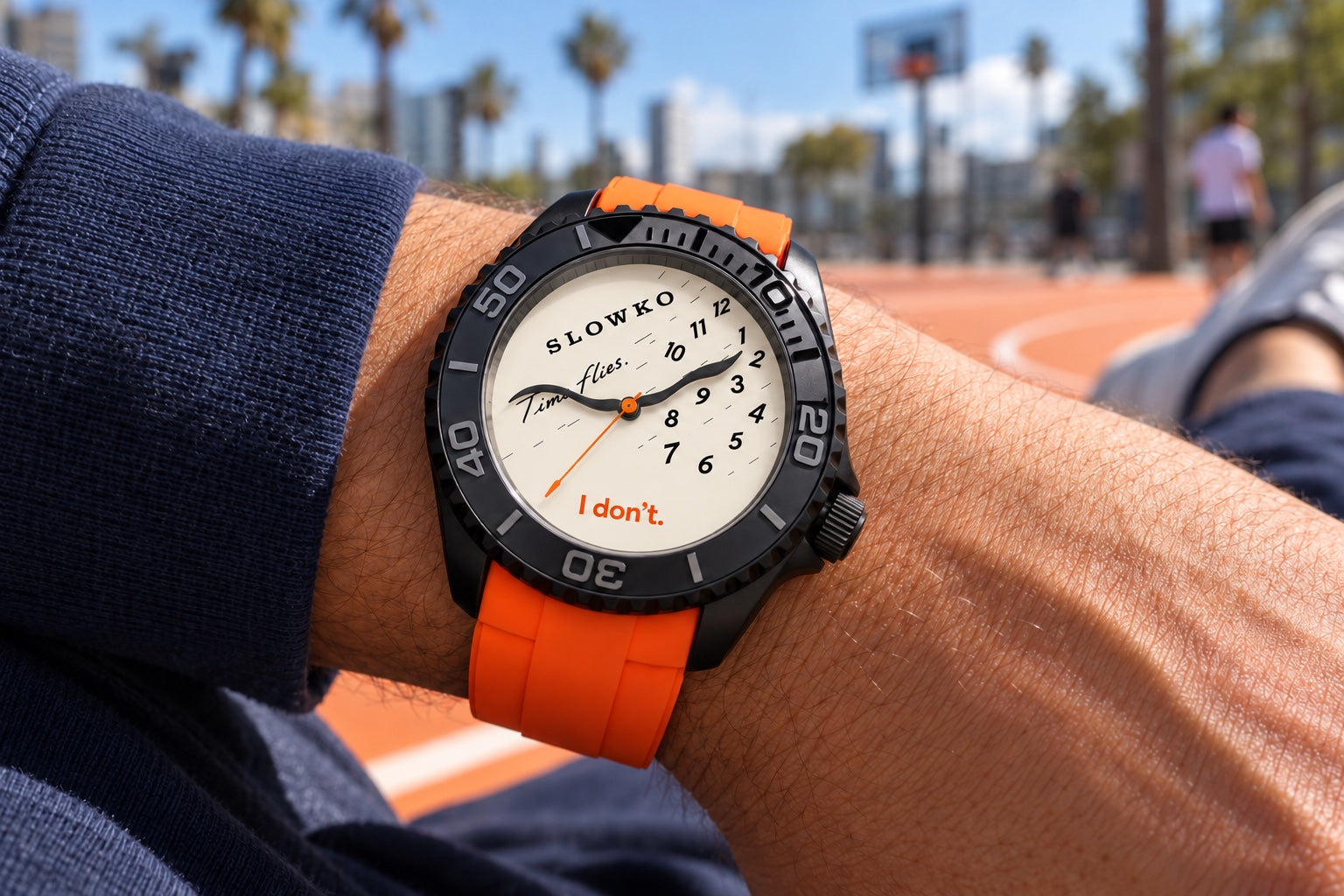 A relaxed wrist wearing SLOWKO with its bright orange rubber strap in the afternoon sun.
